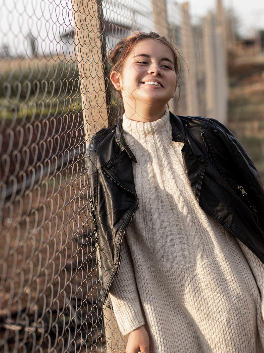 A woman laughing in warm outdoor light beside a fence
