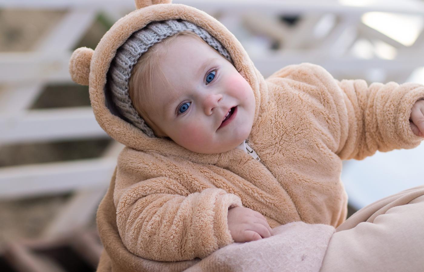 A baby in a soft bear suit looking toward the camera