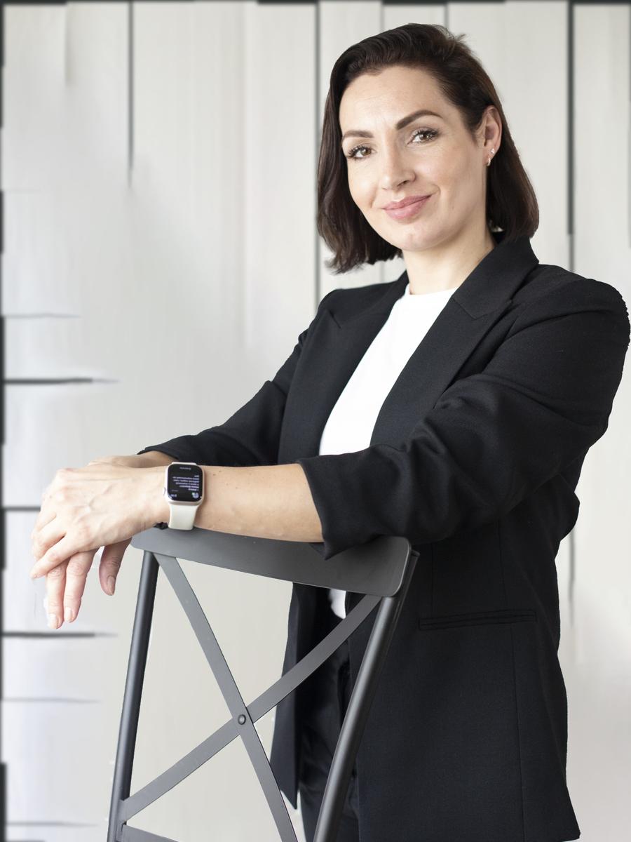 Professional woman in a black blazer posed against a bright modern wall