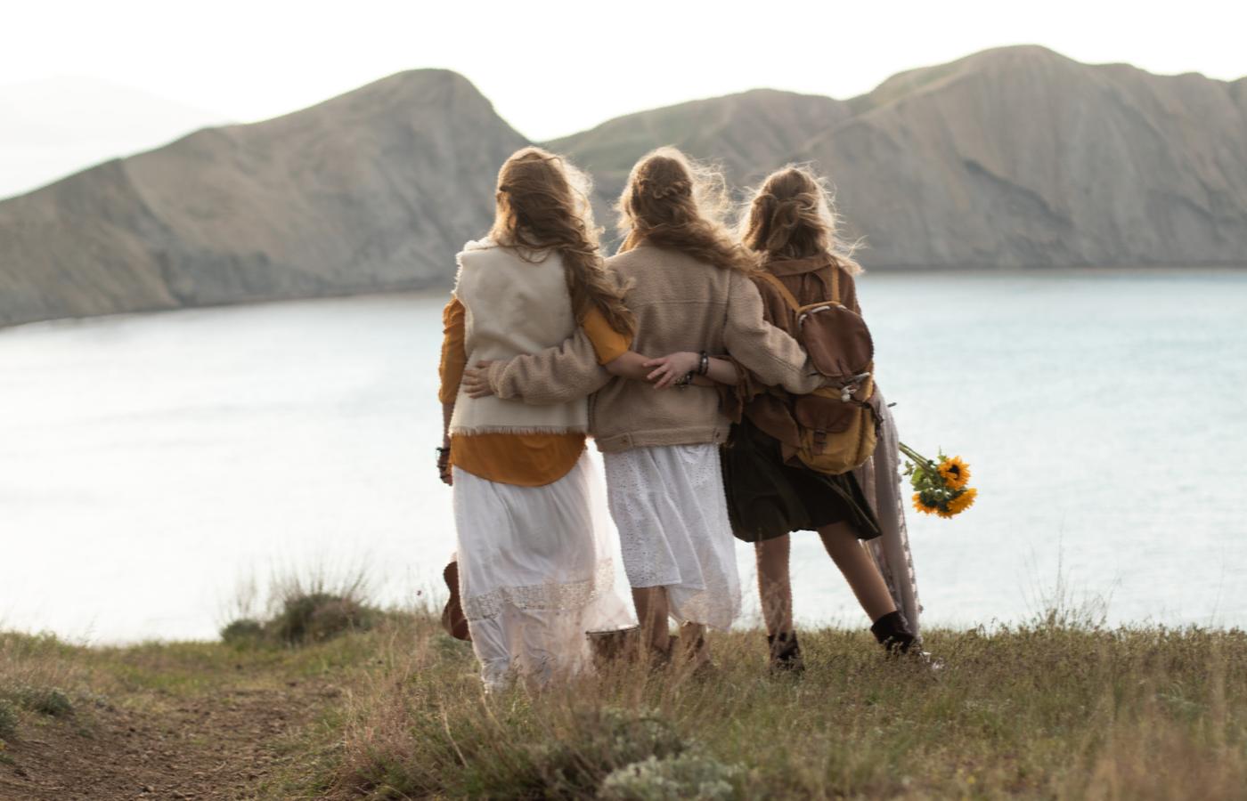 Three women standing arm in arm beside a mountain lake