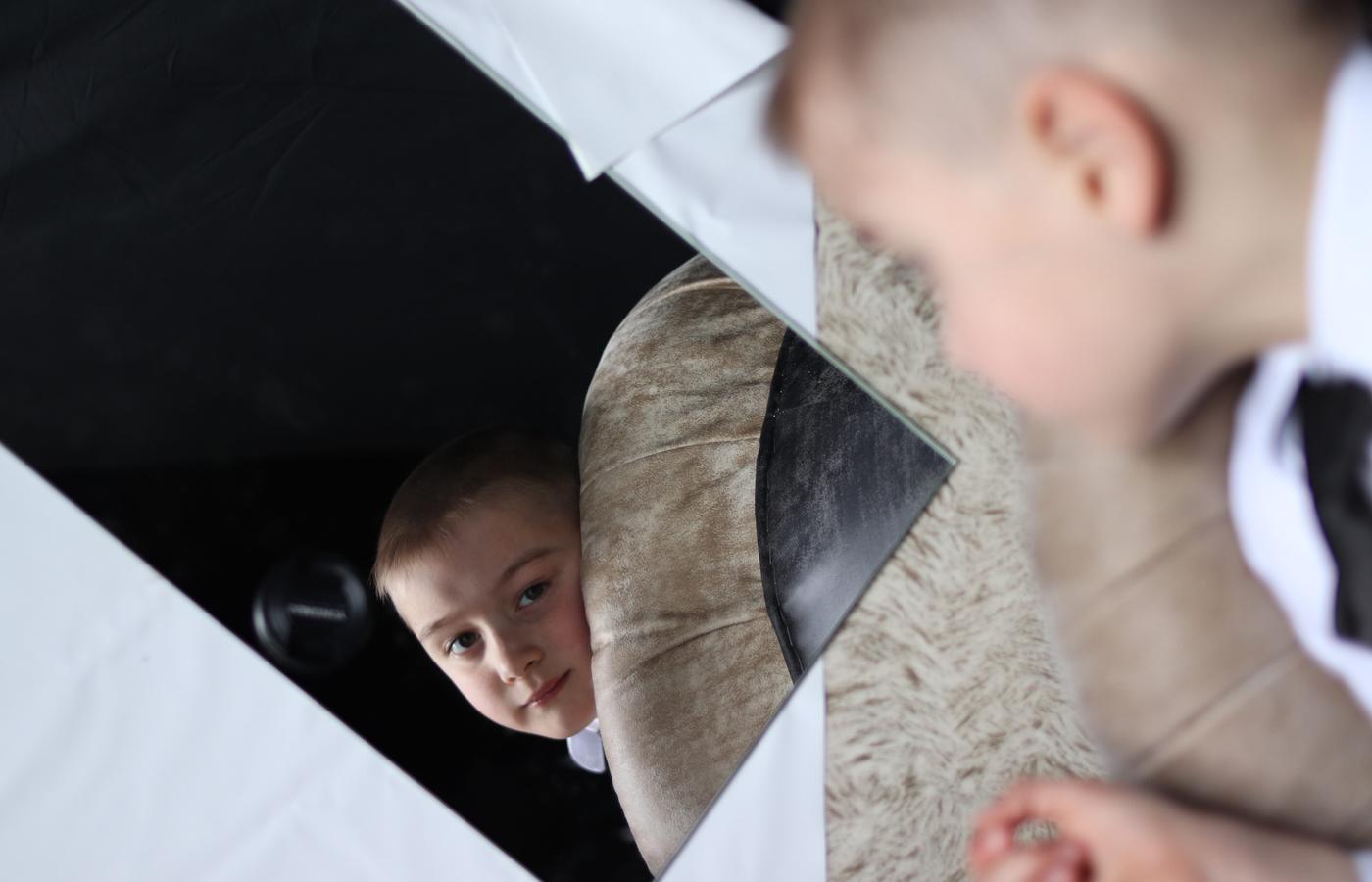 A boy peering through angled mirrors against a black background