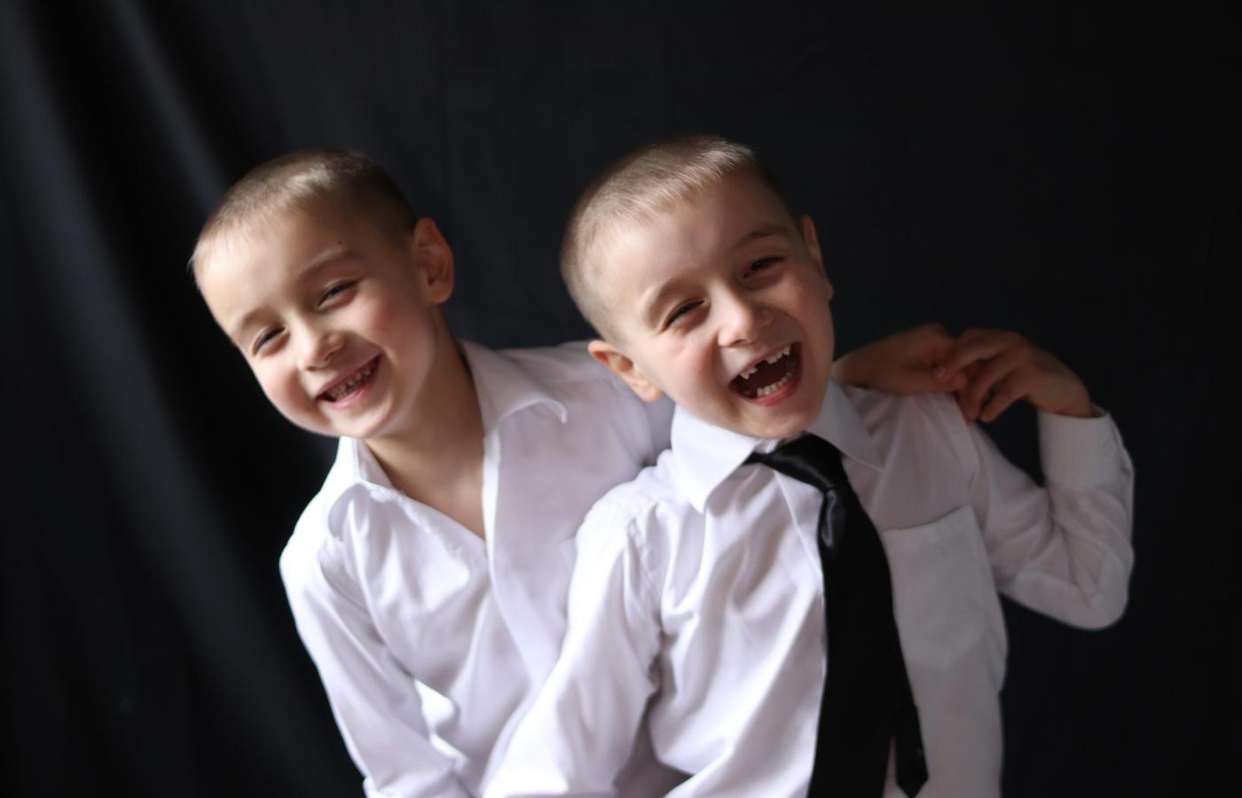 Two brothers laughing together against a black background