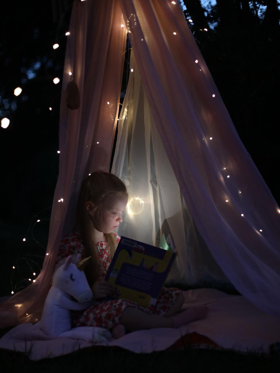 A child reading inside a dark tent lit with tiny lights