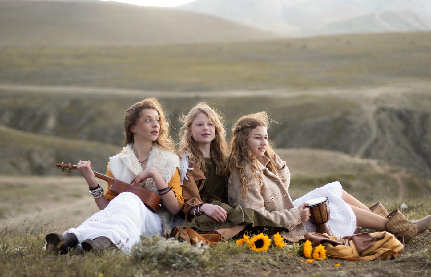 Three women seated with instruments and sunflowers in the mountains