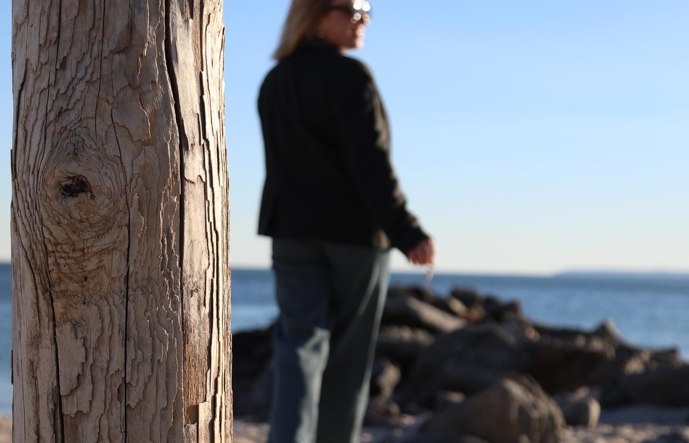 Woman walking along the beach framed by a weathered wooden post