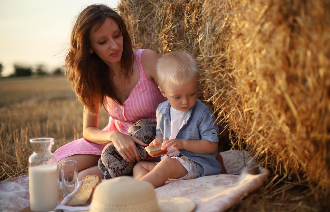 A mother and young child sharing a picnic beside hay bales