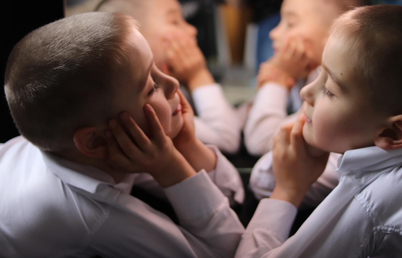 Two boys facing one another through a set of mirrors