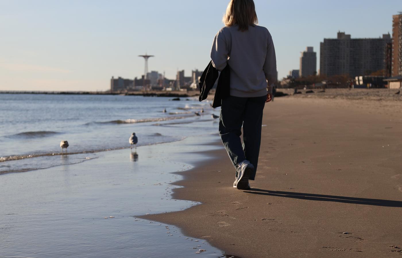 Woman walking the Coney Island shoreline with the Parachute Jump in the distance