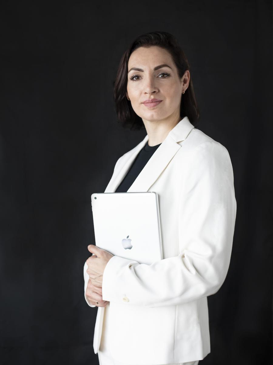 Professional woman in a white blazer holding a tablet against a black backdrop