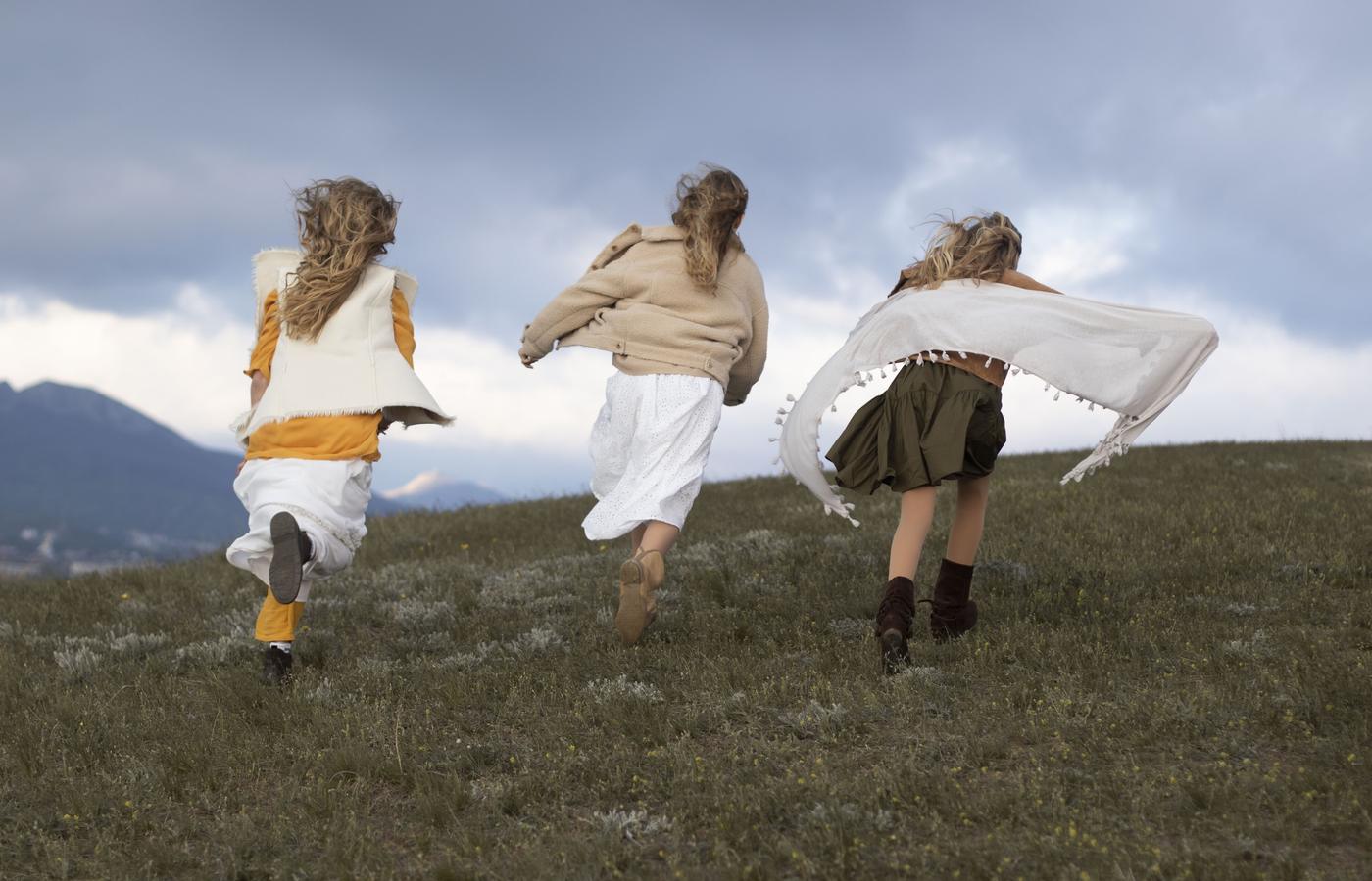 Three women running over a ridge beneath a stormy sky