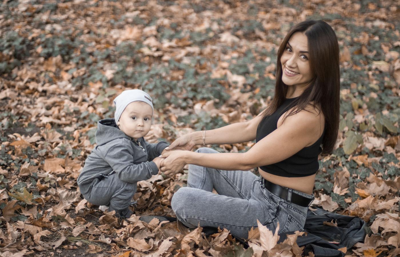 A mother sitting with her baby among autumn leaves