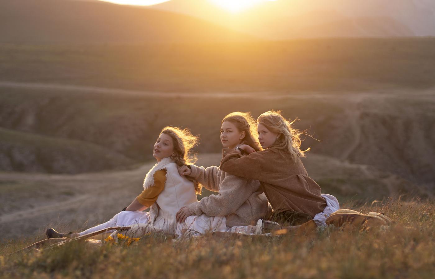 Three women gathered on a hillside in glowing evening light