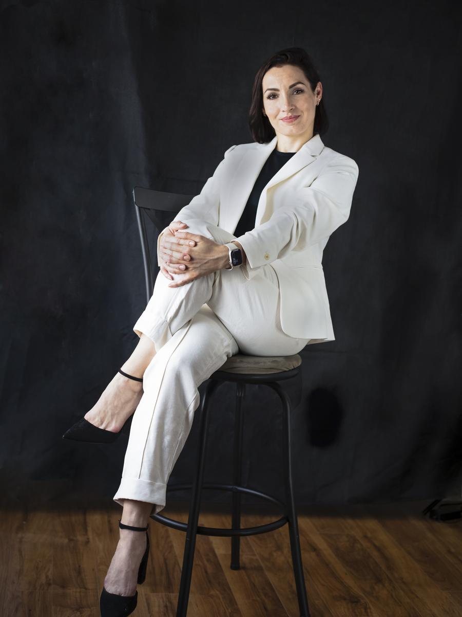 Professional woman in a white suit seated on a stool in a studio