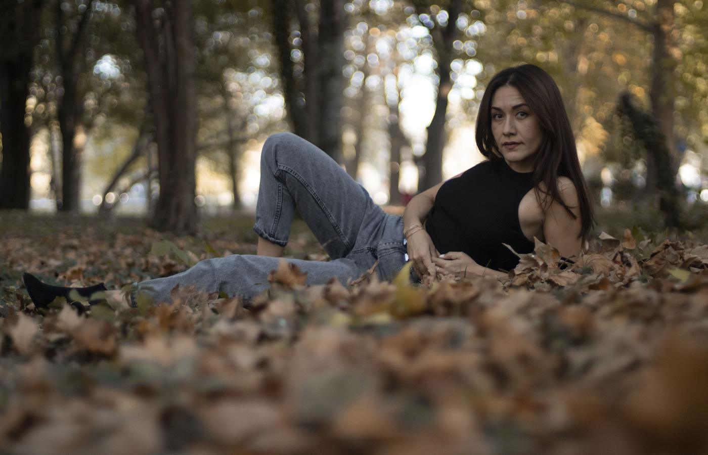 A woman seated among leaves in a shadowed forest portrait