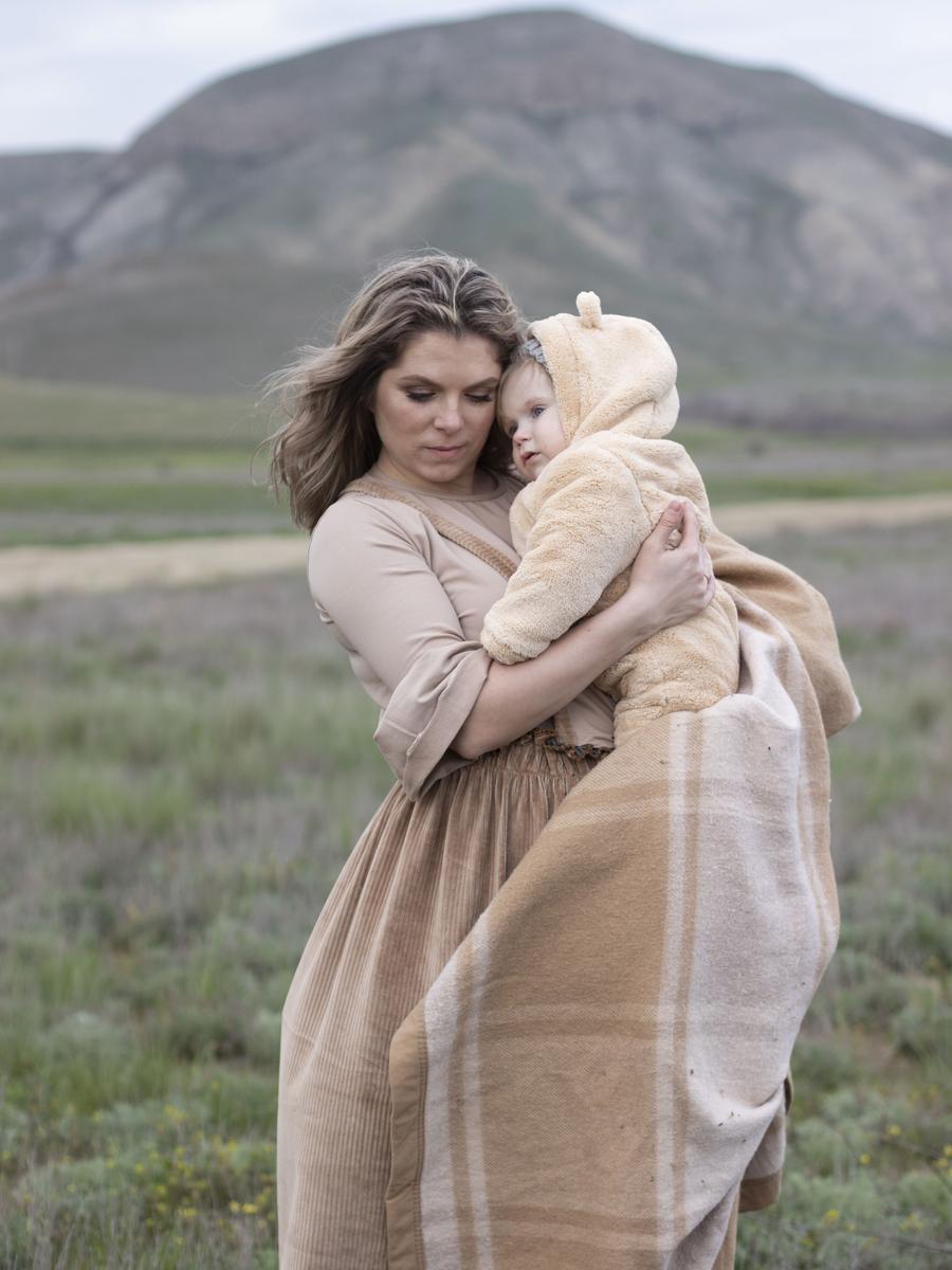 A mother holding her small child close in a green mountain landscape