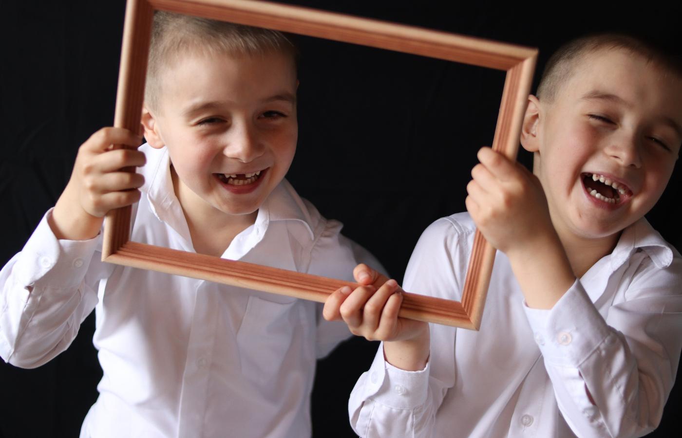 Two laughing brothers leaning through a wooden picture frame
