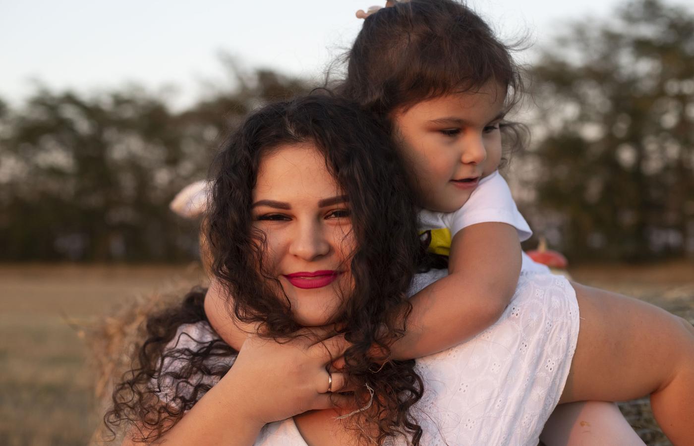 A mother carrying her laughing daughter through a field