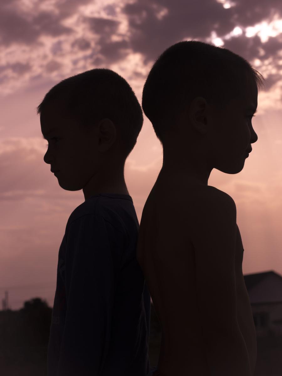 Two brothers standing together outdoors in the last light of day